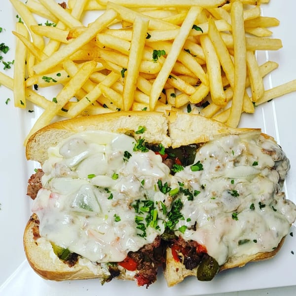 A Jasmine Grill and Kabab cheesesteak sandwich with melted cheese, peppers, and onions, served with fries.