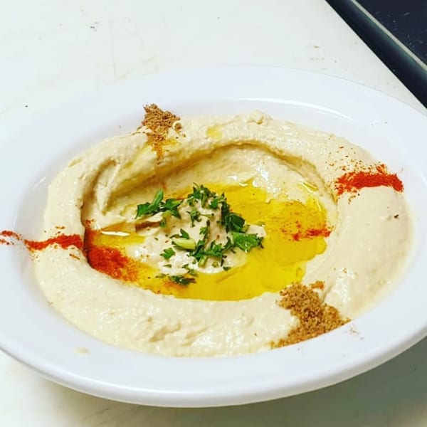 Creamy hummus drizzled with olive oil, garnished with parsley, paprika, and cumin in a white bowl.